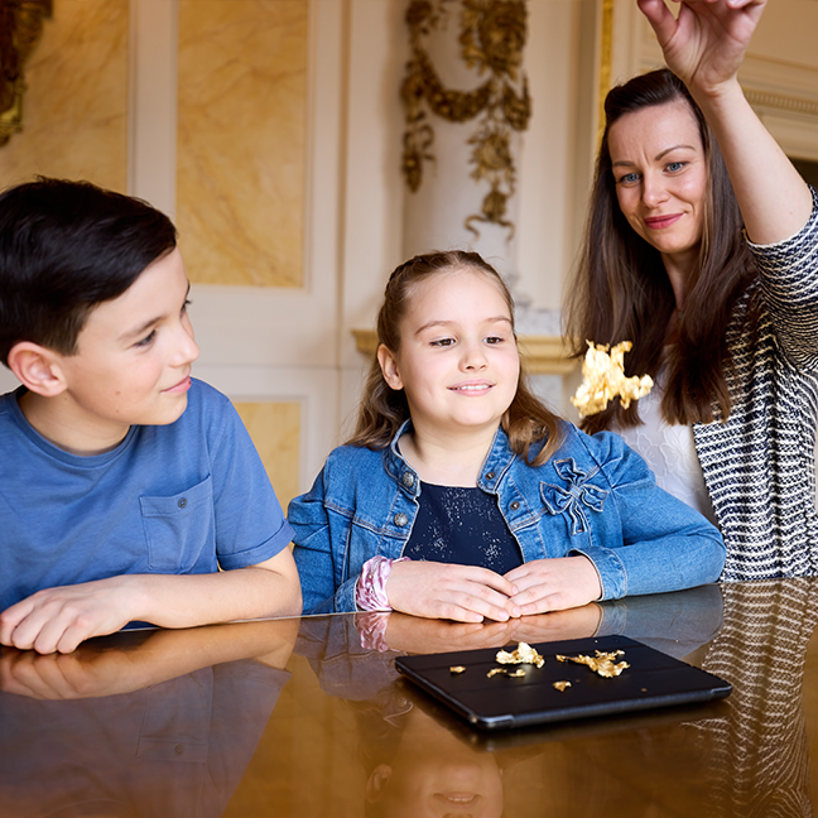 Eine Gruppe von Kindern steht in einem prachtvollen Raum, während eine Führerin ihnen einen Gegenstand zum Riechen hinhält und sie in eine sinnliche Lernaktivität einbindet.