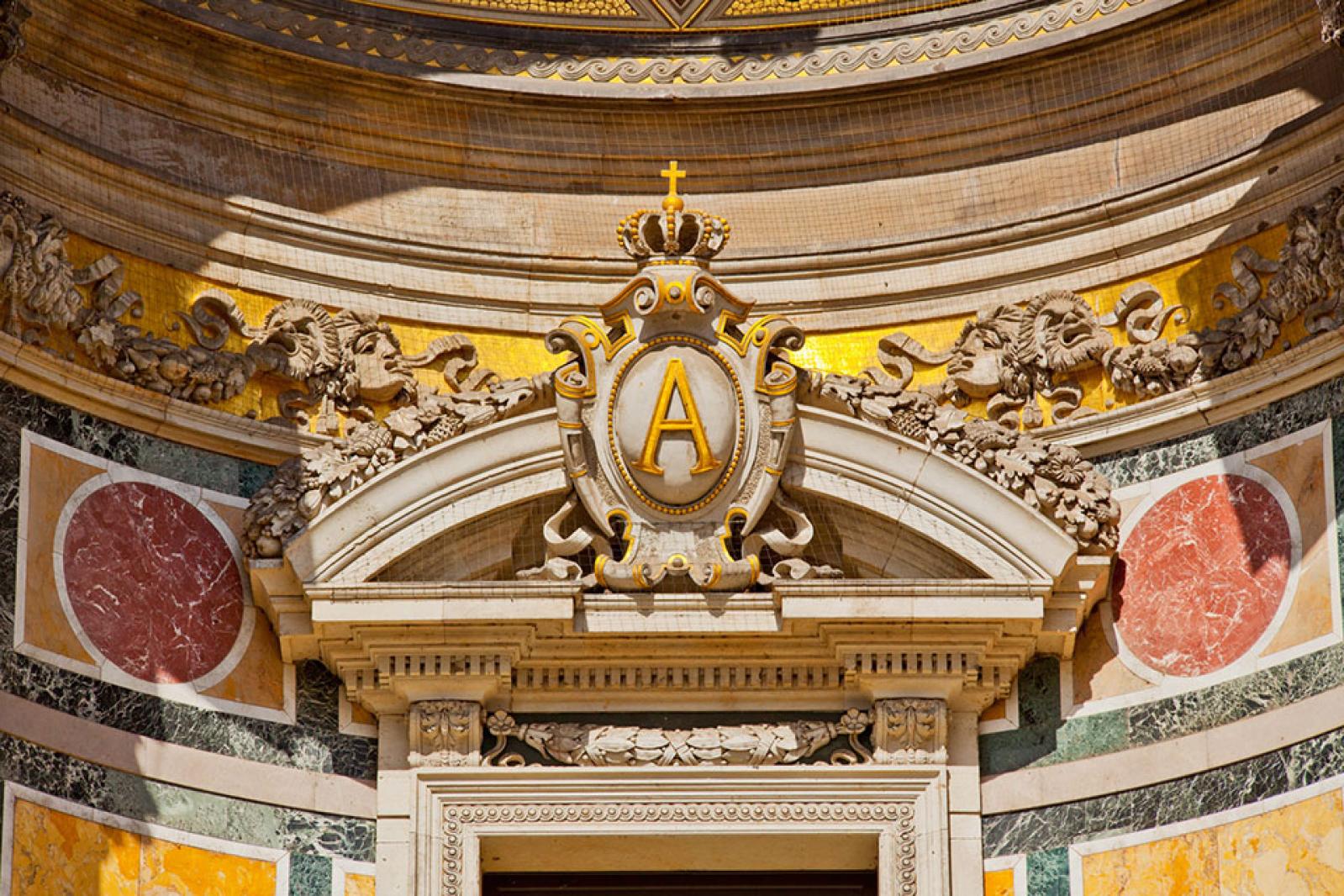 Ein kunstvolles Architekturdetail an der Fassade der Semperoper mit einem bekrönten Buchstaben „A“ in einem dekorativen Wappen, umgeben von Skulpturen, Marmoreinlagen und goldenen Akzenten.