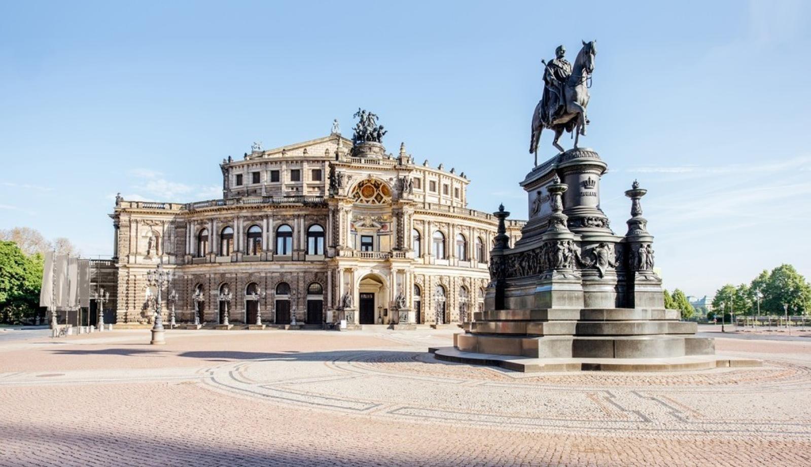 Die Semperoper in Dresden erstrahlt an einem winterlichen Abend im Schnee, mit leuchtenden Laternen und dem Reiterstandbild im Vordergrund.