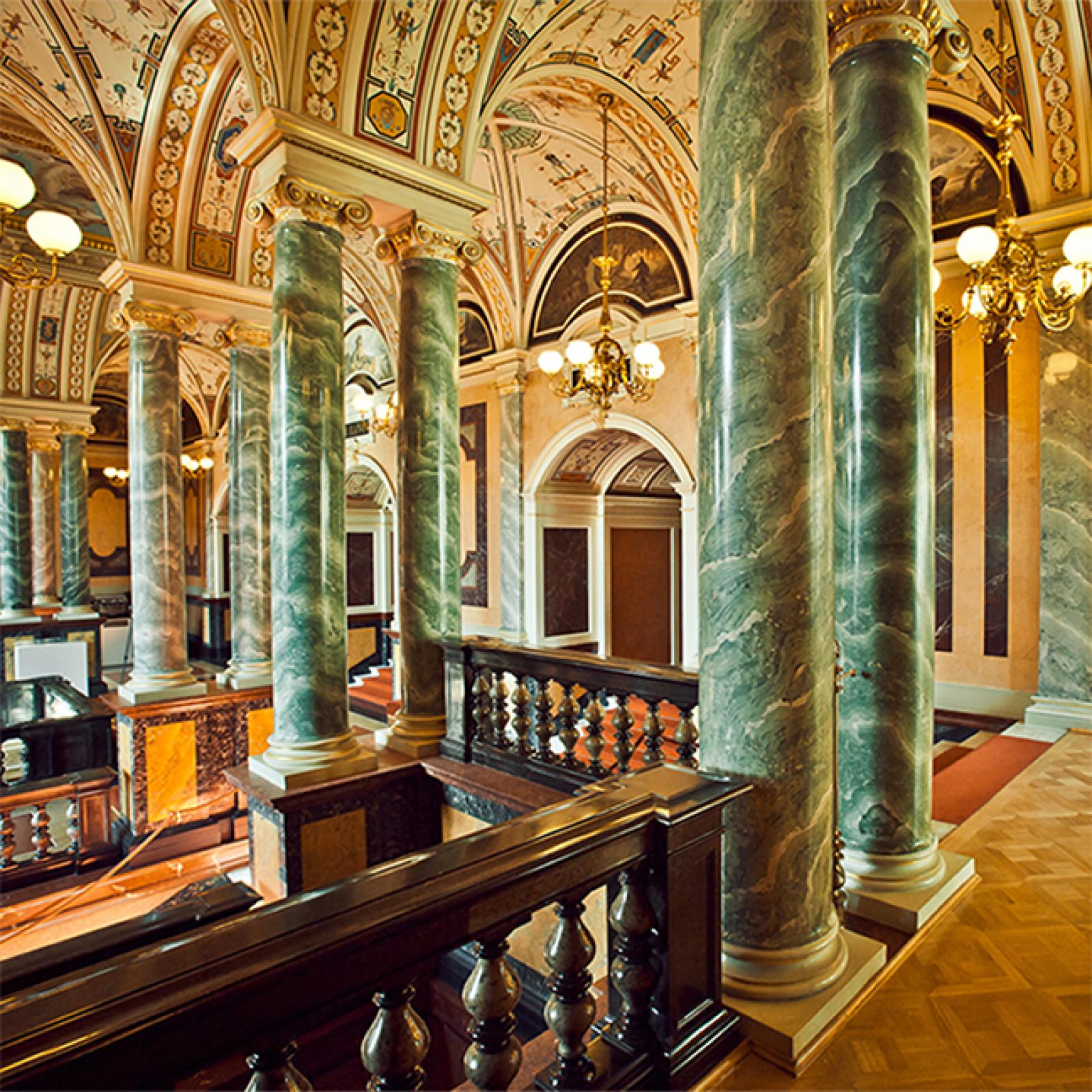Prunkvolles Interieur mit hohen grünen Marmorsäulen, verzierten Bögen, Kronleuchtern und kunstvoll bemalten Decken in einem historischen Opernhaus.