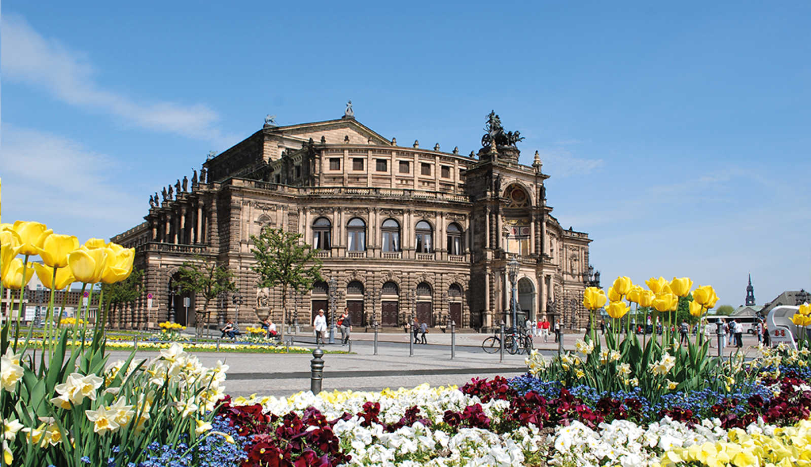 Die Semperoper in Dresden erstrahlt an einem winterlichen Abend im Schnee, mit leuchtenden Laternen und dem Reiterstandbild im Vordergrund.
