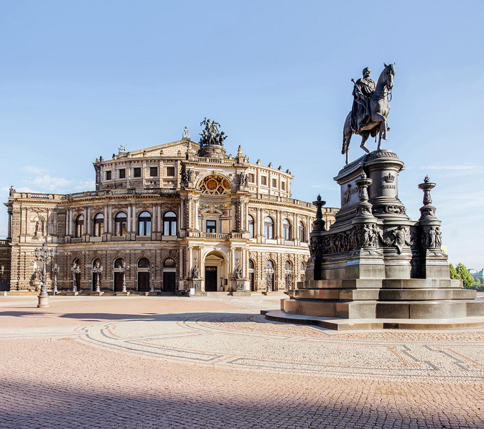 Die Semperoper in Dresden erstrahlt an einem winterlichen Abend im Schnee, mit leuchtenden Laternen und dem Reiterstandbild im Vordergrund.
