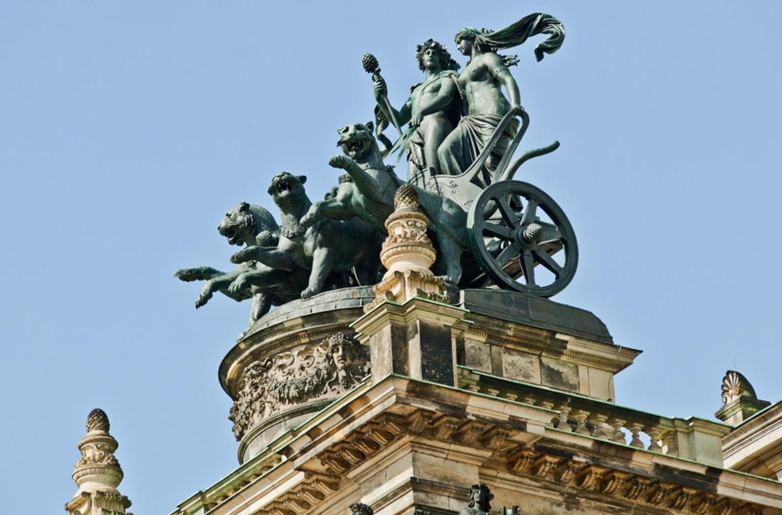 Die Quadriga auf dem Dach der Semperoper zeigt mythologische Figuren auf einem von Panthern gezogenen Wagen, vor einem klaren blauen Himmel.