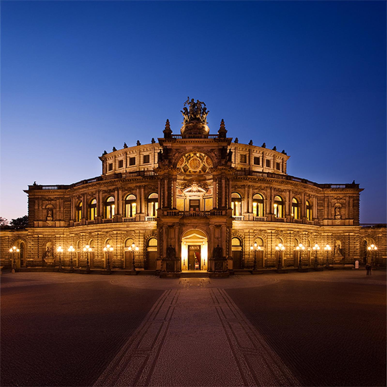 Die Semperoper in Dresden bei Nacht, stimmungsvoll beleuchtet mit warmem goldenem Licht vor einem tiefblauen Abendhimmel.