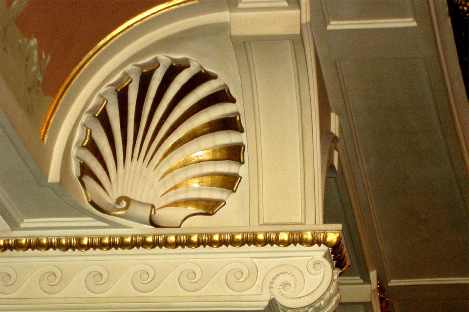 Detailaufnahme eines kunstvollen Muschelmotivs im Inneren der Semperoper, mit weißem Stuck, goldenen Akzenten und klassizistischen Verzierungen.