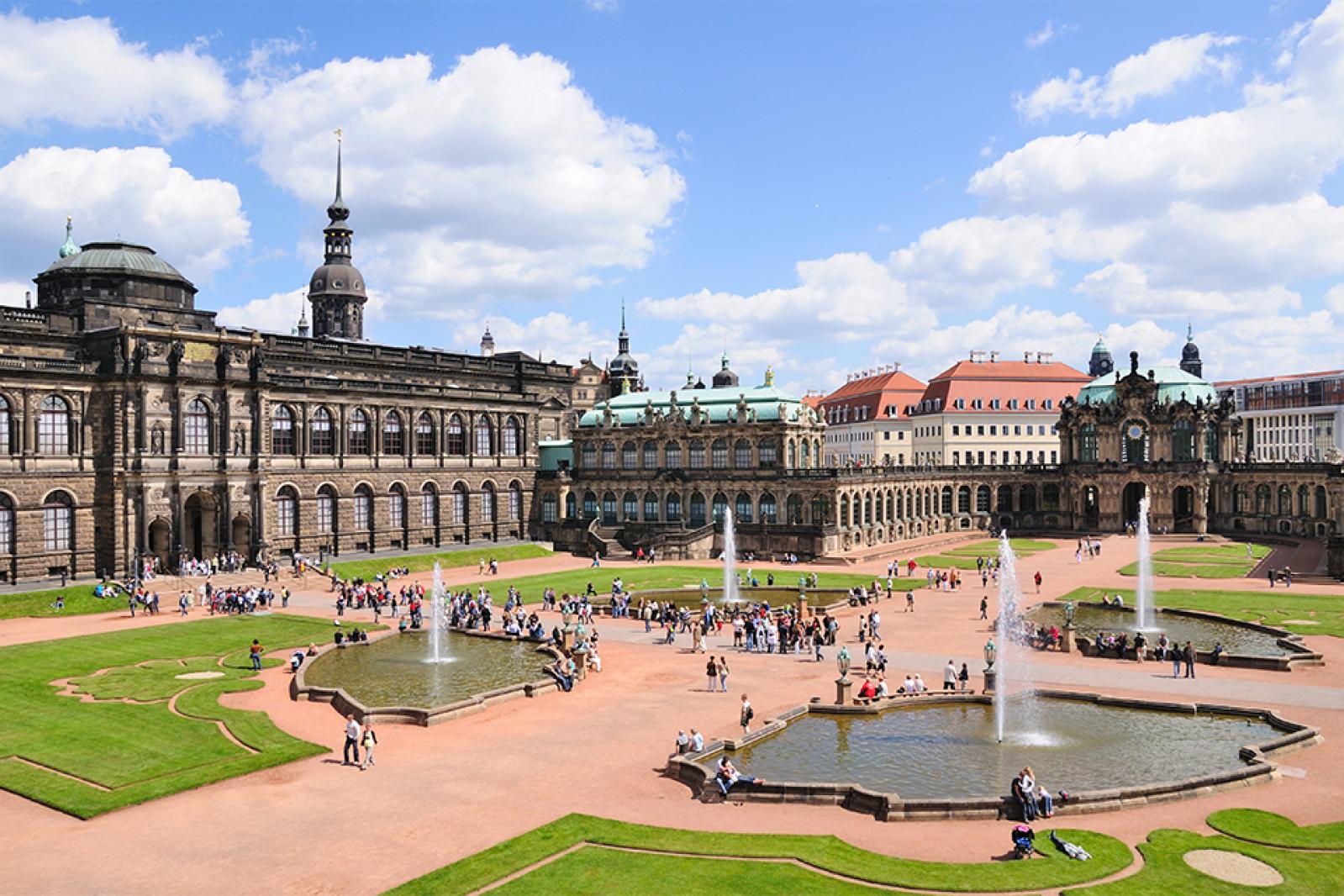 Der Dresdner Zwinger mit seinen barocken Gebäuden, Brunnen und gestalteten Innenhöfen, belebt von zahlreichen Besuchern bei blauem Himmel.