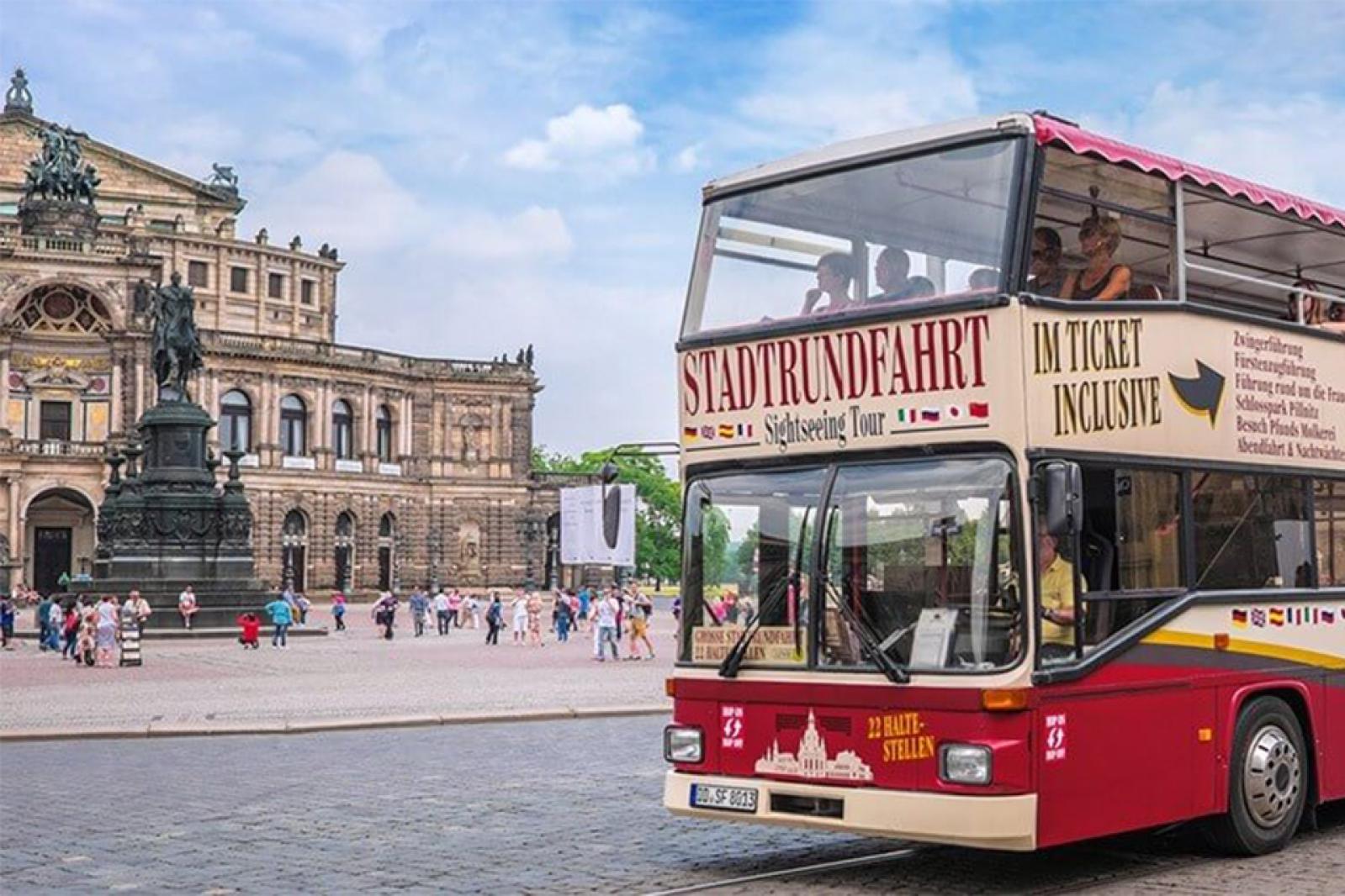 in roter Doppeldecker-Stadtrundfahrtbus hält am Theaterplatz in Dresden, im Hintergrund die Semperoper und das Reiterstandbild.